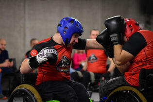 dwóch mężczyzn na wózkach walczący w sali sportowej w ochraniaczach i rękawicach bokserskich 
