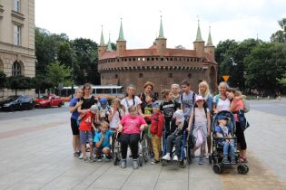 Zdjęcie przedstawia grupę dzieci pozujących do zdjęcia na placu Matejki w Krakowie