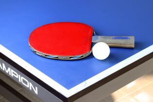 Zdjęcie przedstawia paletkę do tenisa stołowego z piłką do tenisa stołowego leżące na stole do tenisa stołowego