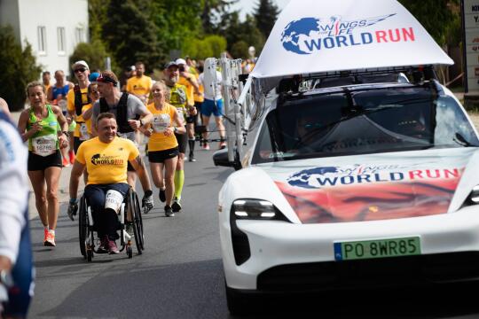 fotografia przedstawia maratończyków przebiegających obok samochodu 