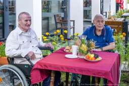 Na zdjęciu dwóch mieszkańców siedzących przy stoliku podczas Rycerskiego Pikniku Jubileuszowego w ogrodzie Domu. 