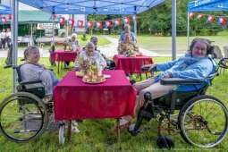 Na zdjęciu mieszkanki siedzące przy trzech stolikach podczas Rycerskiego Pikniku Jubileuszowego. 