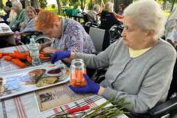 Na zdjęciu jedna mieszkanka podczas krojenia marchwi, oraz druga mieszkanka, która wkłada marchew do słoika w ogrodzie DPS Praska 25.