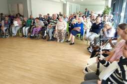 Na zdjęciu mieszkańcy siedzący w dużej grupie tuż przed występem dziewcząt z Państwowej Szkoły Muzycznej I stopnia im. Michała Kleofasa Ogińskiego w Miechowie. 