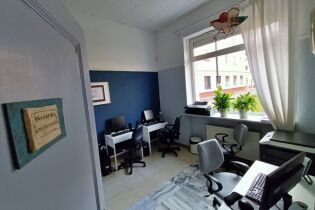 fotografia przedstawia wnętrze pracowni komputerowej. Widzimy biurka ustawione przy ścianach a na nich monitory. przy biurkach stoją fotele biurowe.