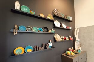 Fotografia przedstawia półki a na nich wyeksponowane różne wielobarwne wyroby ceramiczne.