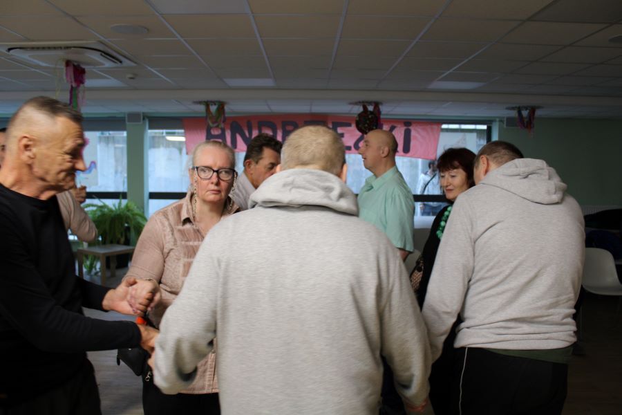 Grupa tańczących kobiet i mężczyzn w pomieszczeniu.