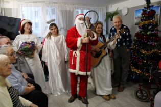 Grupa kobiet i mężczyzn zgromadzonych przy udekorowanej choince. Na pierwszym planie osoby.