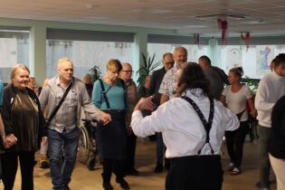 Grupa tańczących kobiet i mężczyzn w pomieszczeniu. W tle projekcja na ekranie.