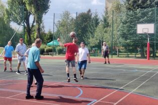 Drużyna mężczyzn w strojach sportowych rozgrywa mecz piłki możnej na boisku sportowym. Jeden z zawodników wybija piłkę głową.