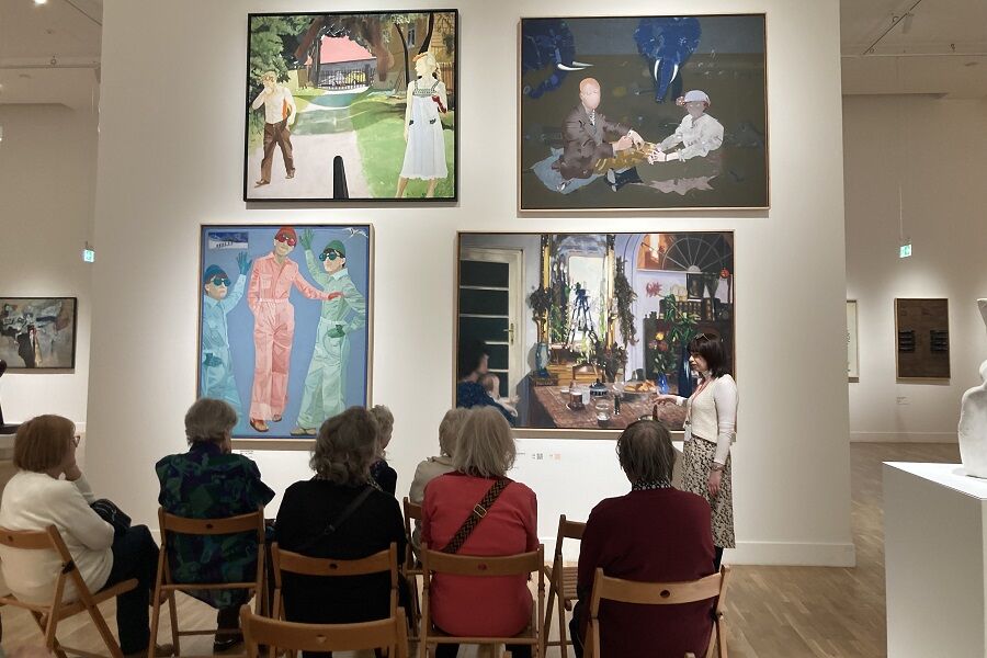 Zdjęcie przedstawia seniorów oglądających obrazy oraz Panią przewodnik która tłumaczy tematykę wybranych dzieł.