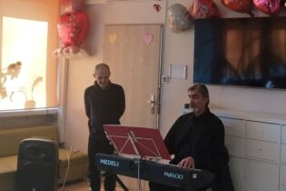 Dwaj mężczyźni, jeden stoi, drugi siedzi i gra na instrumencie klawiszowym