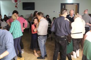 Grupa tańczących osób w pomieszczeniu udekorowanym serduszkami.