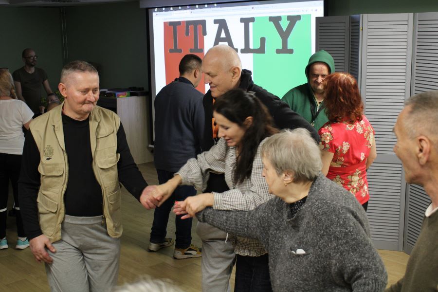 Grupa tańczących kobiet i mężczyzn w pomieszczeniu.