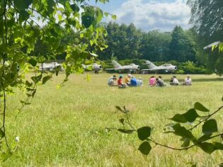 Uczestnicy odpoczywają na trawie wśród olbrzymich maszyn 