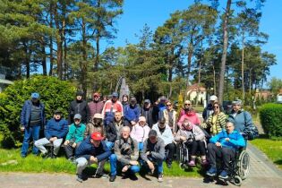 Grupa osób pozuje do zdjęcia na tle zielonych drzew w słoneczny dzień.