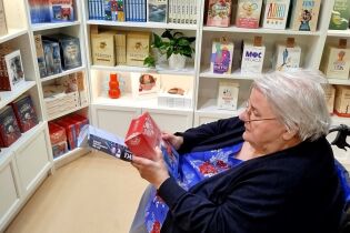 Kobieta siedzi na wózku, przegląda książki w księgarni. W tle półki pełne książek o różnorodnej tematyce.