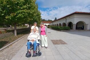 Na zdjęciu troje mieszkańców na terenie placu Bazyliki Krzyża Świętego przy alejce drzew. 