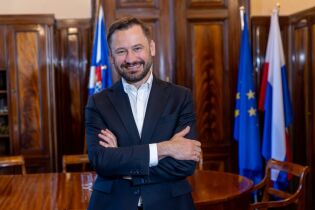 mężczyzna w granatowym garniturze stoi z założonymi ramionami i uśmiecha się