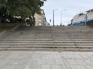 Schody prowadzące w górę, otoczone drzewami i budynkami.